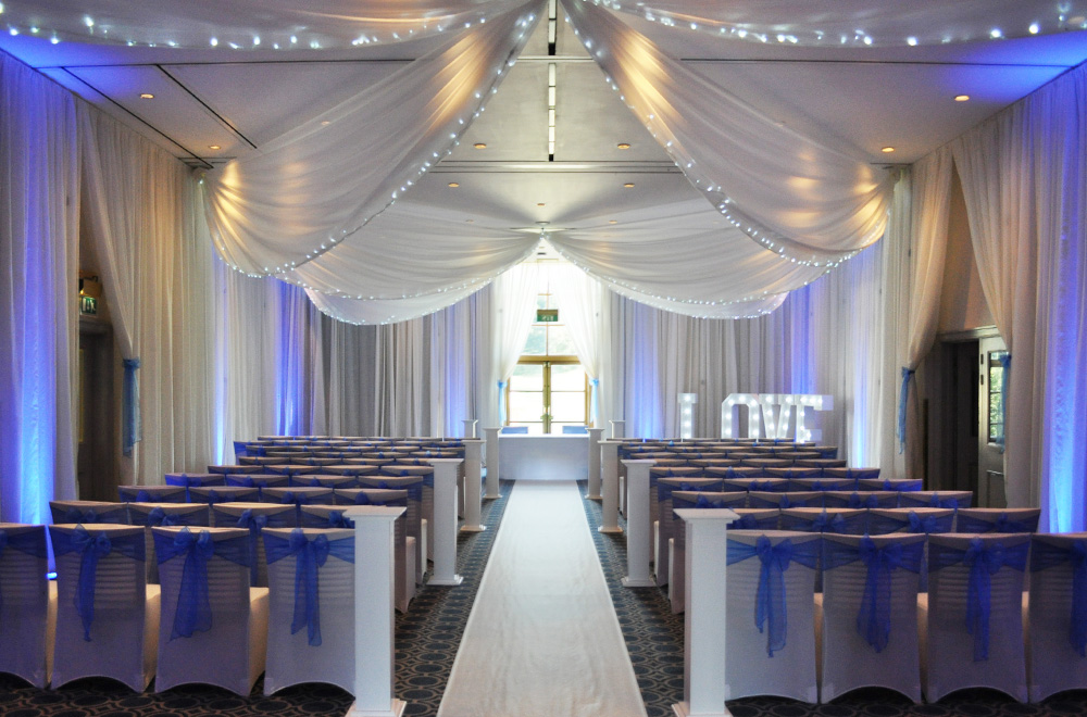 Wall and Ceiling drapes for a wedding ceremony with Blue chair sashes and uplighting on the drapery at Bowood Hotel spa and Golf Club