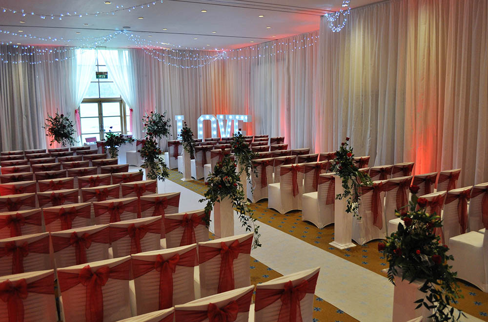 Red uplighting and chair cover sashes with full room drapes and white aisle runner at a wedding at Bowood Hotel, spa and gold club.