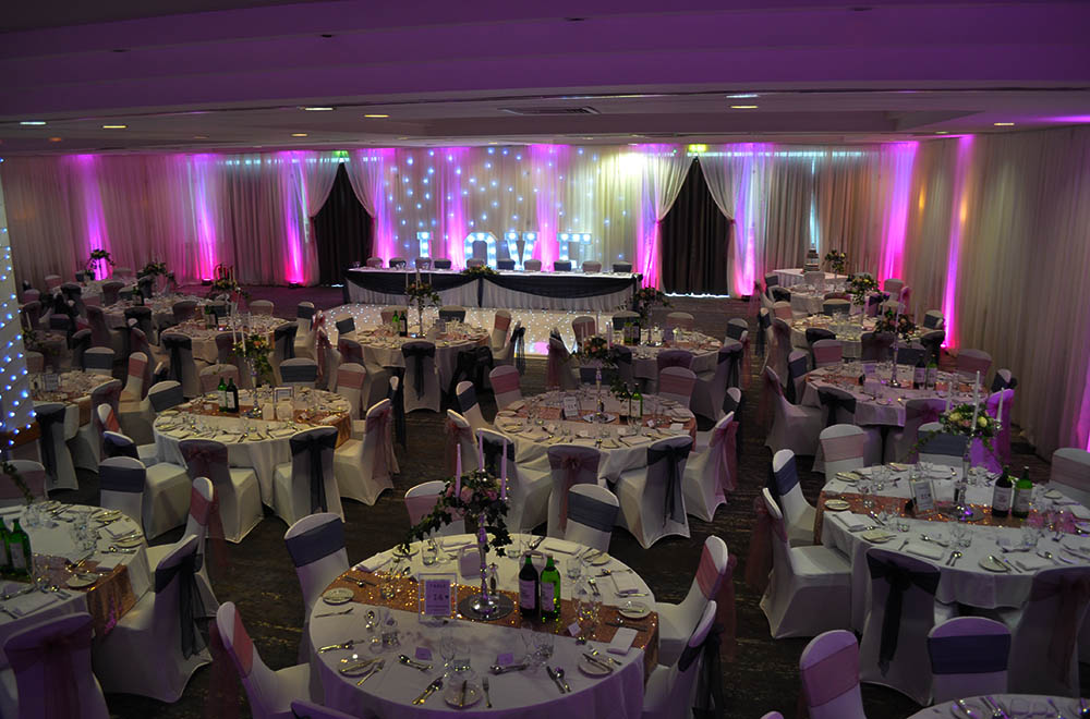 Pink and purple uplighters with room wall drapes for a wedding breakfast at the Double Tree Hilton Hotel in Swindon