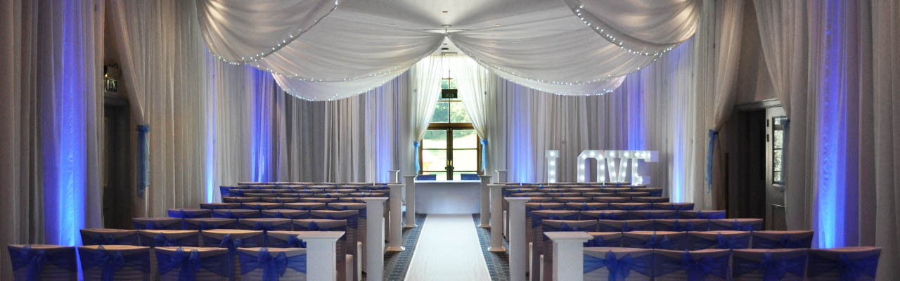 Wedding drapes, LED LOVE letters, chair covers with blue sashes and uplighting. Full room wall and ceiling drapes with fairy lights for a wedding ceremony at Bowood Hotel spa and Golf Club with white roman pillars