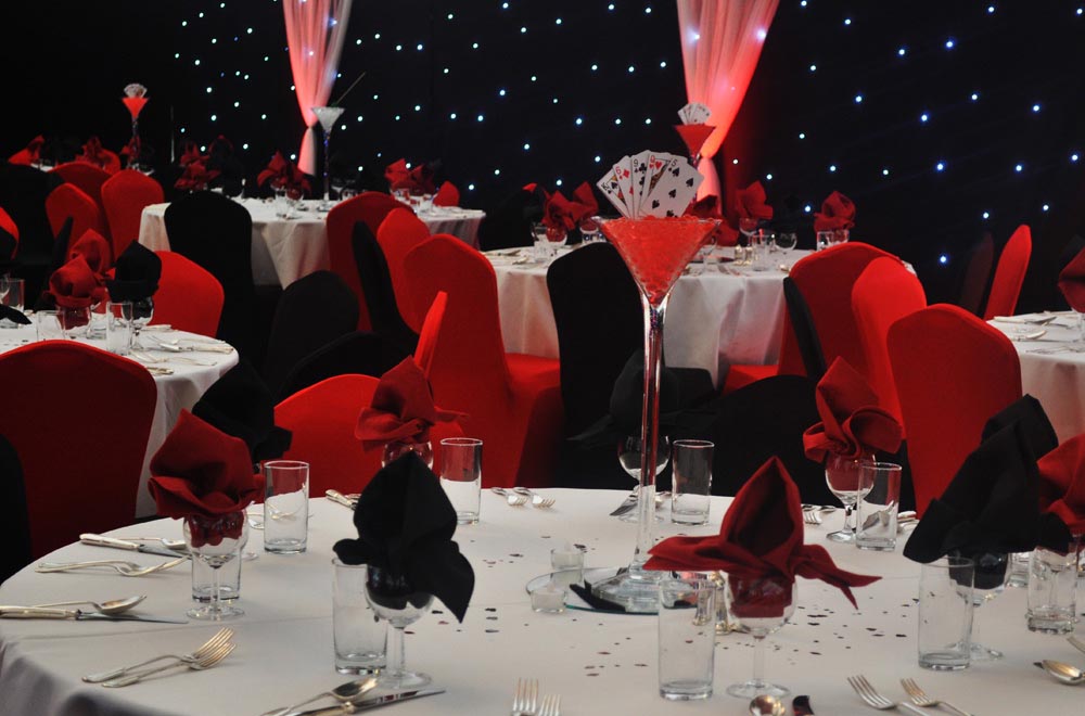Red anc black themed corporate event with chair covers and black starlit starcloth backdrop and martini glass centre pieces