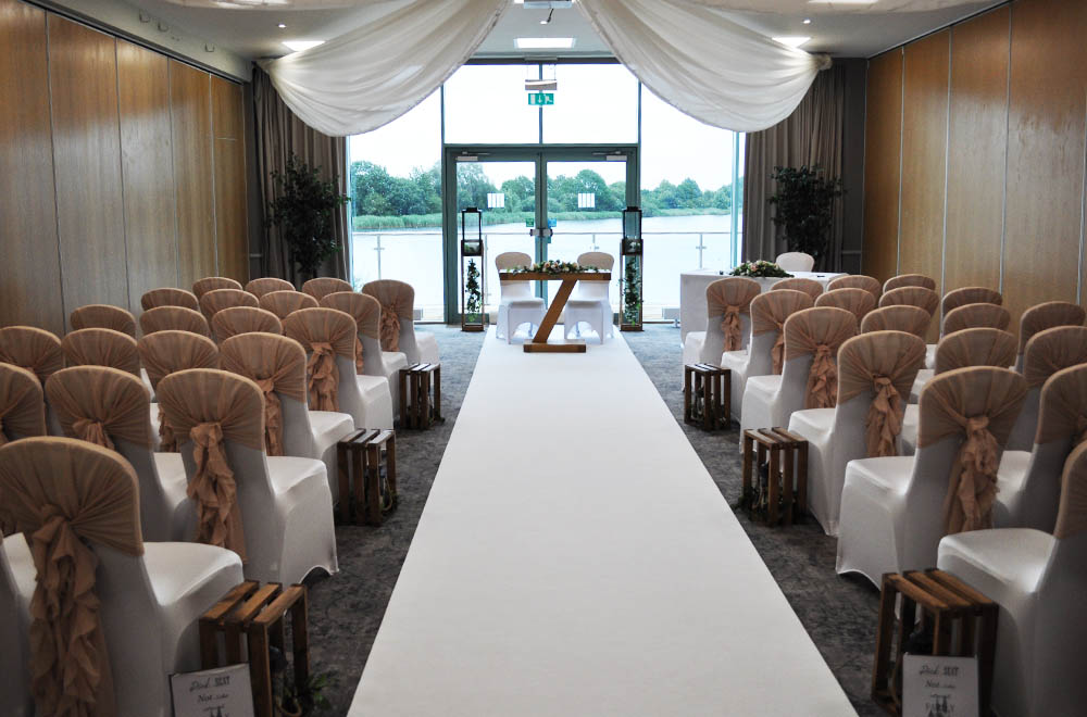 Blush pink ruffle hoods on wedding chair covers for a ceremony with ceiling drapes at De Vere Cotswold Waterpark Hotel