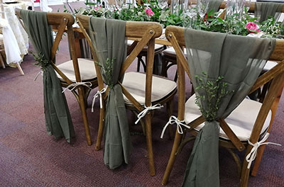Rustic cross-back chairs with moss coloured chiffon chair drops and foliage