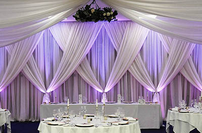 Purple and Blue uplighting on crossed wall drapes and hanging floral arrangement from ceiling drapes