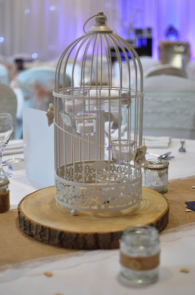 White Birdcage wedding table centrepiece on a wooden log slice