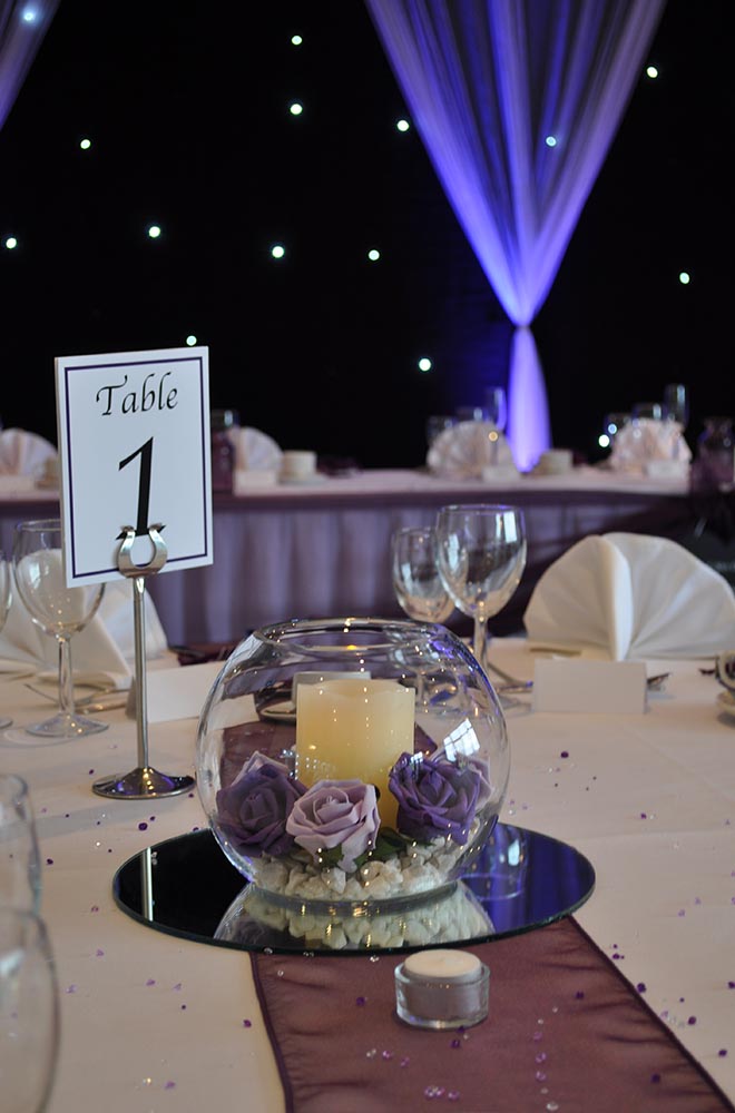 Fishbowl wedding centre piece with artificial flower heads and candles in purple